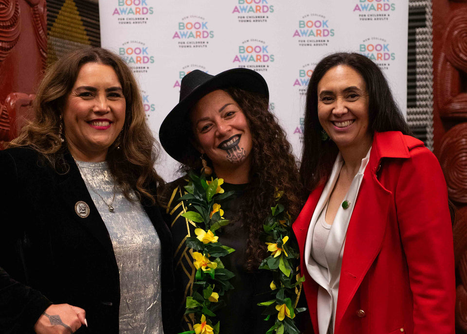 Pania Tahau-Hodges, Elizabeth Gray and Eboni Waitere smiling and posing together in front of a 'NZ Children's and Young Adults Book Awards' backdrop